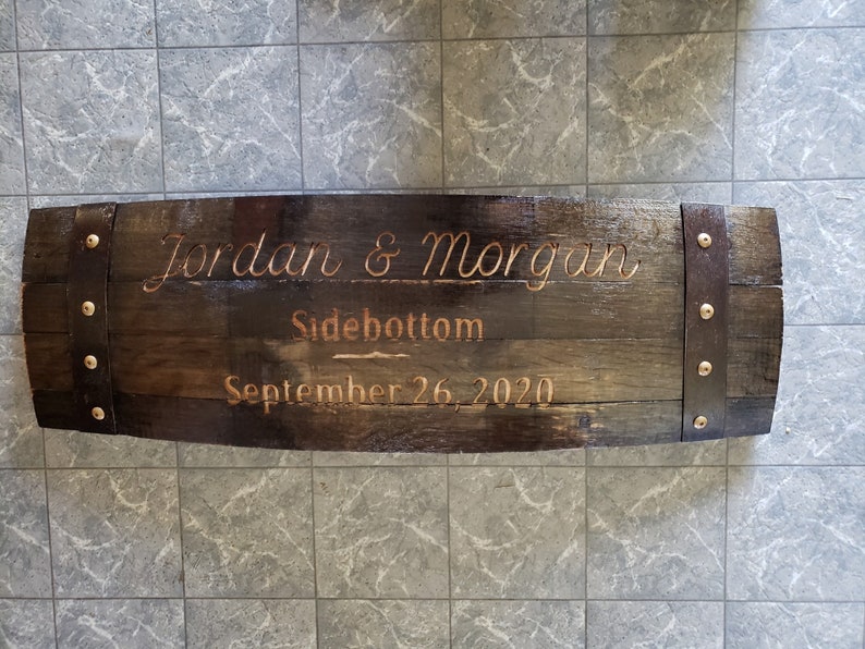 May include: A wooden barrel sign with metal bands and rivets. The sign is engraved with the text "Jordan & Morgan Sidebottom September 26, 2020".