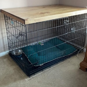 May include: A black metal dog crate with a wooden top. The crate has a green dog bed inside.