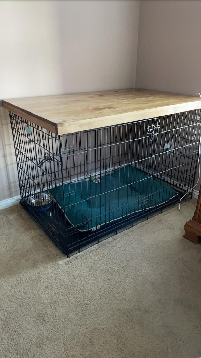 May include: A black metal dog crate with a wooden top. The crate has a green dog bed inside.