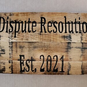 May include: A wooden sign with metal accents and the text "Willett Dispute Resolution, PLLC Est. 2021" in black lettering.