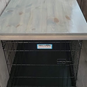 May include: A gray wooden table top with a black metal dog crate underneath. The crate has a black plastic tray and a blue label that says "Precision Pet Products".