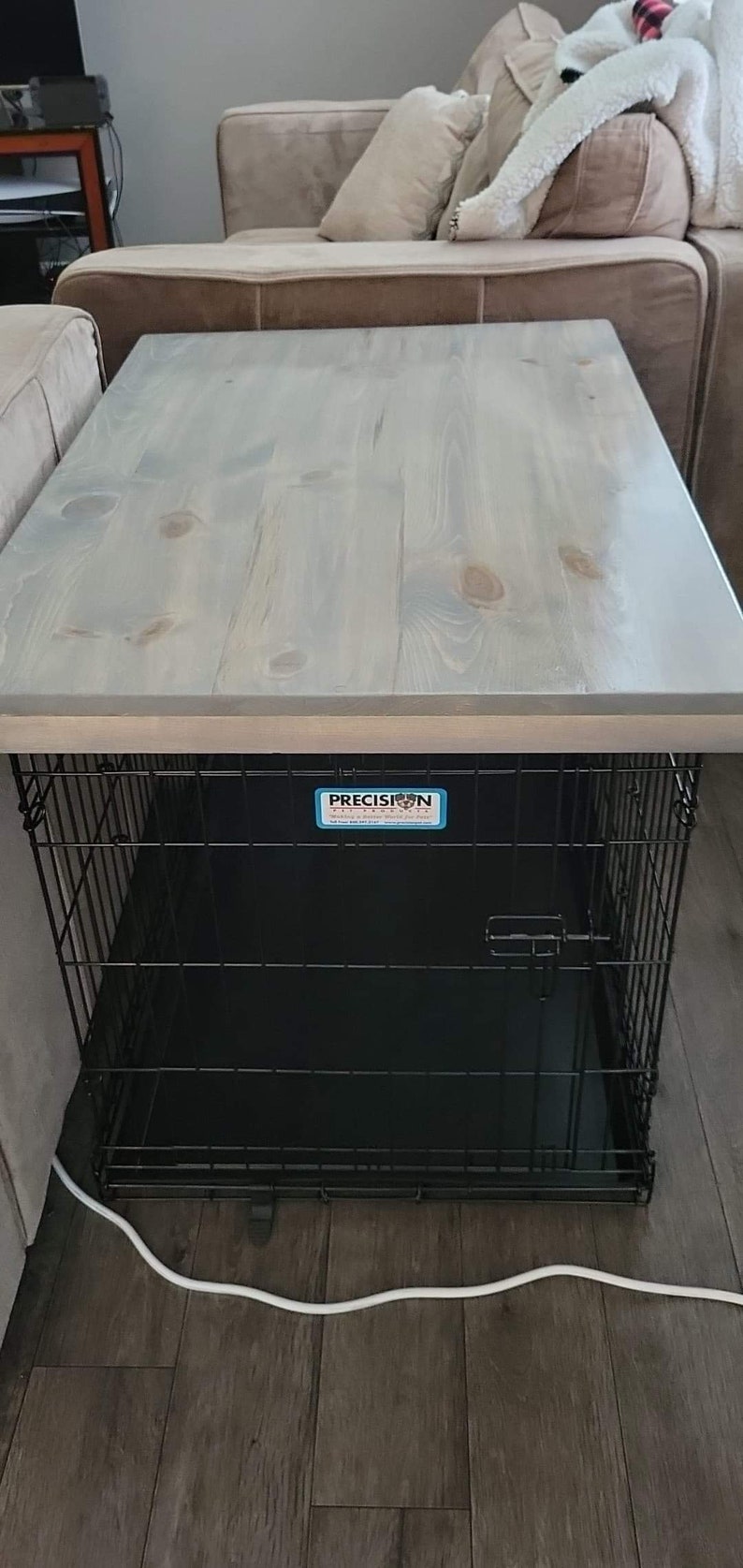 May include: A gray wooden table top with a black metal dog crate underneath. The crate has a black plastic tray and a blue label that says "Precision Pet Products".