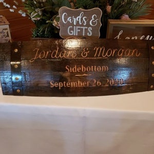 May include: A dark brown wooden barrel with metal accents, engraved with the text "Jordan & Morgan Sidebottom September 26, 2020".