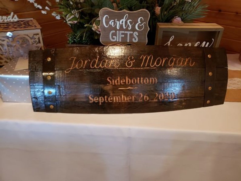 May include: A dark brown wooden barrel with metal accents, engraved with the text "Jordan & Morgan Sidebottom September 26, 2020".