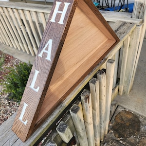 May include: A triangular wooden frame with the word "HAL" spelled out in white letters on the side. The frame is stained a dark brown color and is resting on a wooden railing.