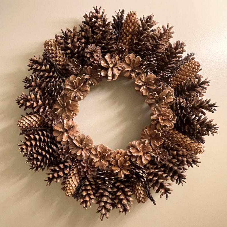 May include: A brown pine cone wreath with a variety of sizes and shapes of pine cones. The wreath is made of natural materials and has a rustic look.