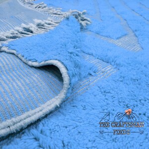 May include: Close-up of a light blue shag rug with a white fringe. The rug has a subtle pattern of white stripes.