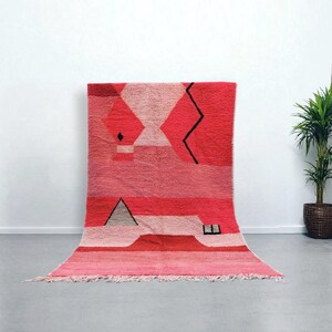 Puede incluir: Una vibrante alfombra geom&eacute;trica en tonos rojos y rosas. La alfombra presenta una serie de formas, incluyendo diamantes, tri&aacute;ngulos y una l&iacute;nea en zigzag, en diferentes tonos de rojo y rosa. La alfombra tiene un borde con flecos.