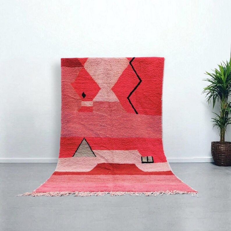 Puede incluir: Una vibrante alfombra geom&eacute;trica en tonos rojos y rosas. La alfombra presenta una serie de formas, incluyendo diamantes, tri&aacute;ngulos y una l&iacute;nea en zigzag, en diferentes tonos de rojo y rosa. La alfombra tiene un borde con flecos.