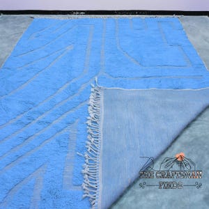 May include: A light blue rug with a geometric pattern. The rug has white fringe around the edges and is folded in half to show the back side.
