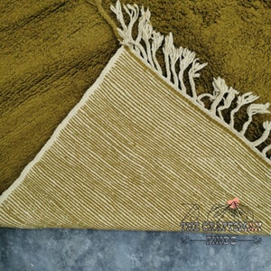 May include: A green and cream woven rug with fringe. The rug is folded in half, showing the underside.