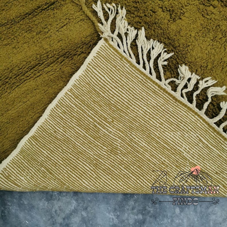 May include: A green and cream woven rug with fringe. The rug is folded in half, showing the underside.