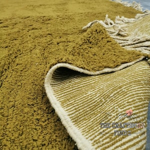May include: Close-up of a mustard yellow rug with a white fringe. The rug has a textured surface and a white and mustard yellow striped backing.