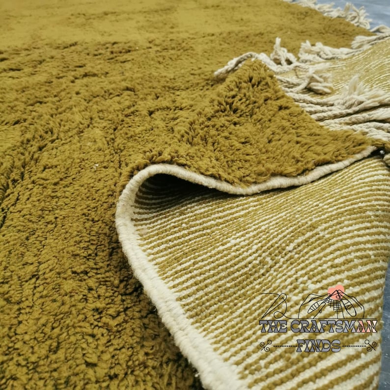 May include: Close-up of a mustard yellow rug with a white fringe. The rug has a textured surface and a white and mustard yellow striped backing.