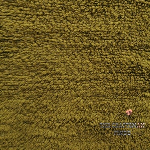 May include: Close-up of a soft, plush fabric in a deep olive green color. The fabric has a fuzzy, textured surface.