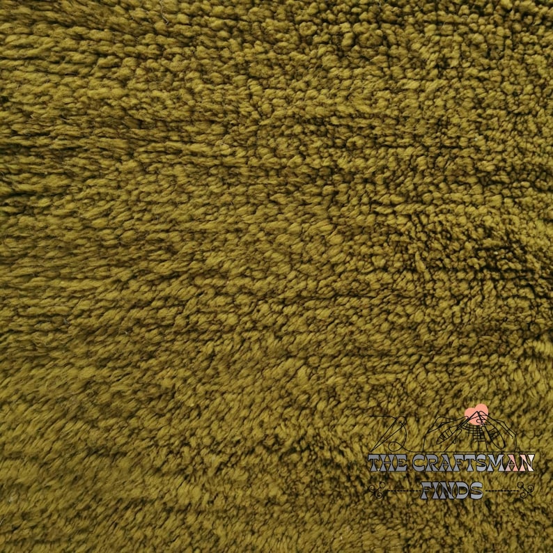 May include: Close-up of a soft, plush fabric in a deep olive green color. The fabric has a fuzzy, textured surface.