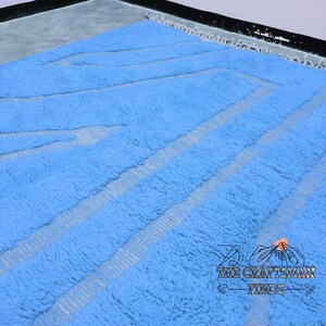 May include: A light blue shag rug with a geometric pattern woven into the fabric. The rug has a fringe border.