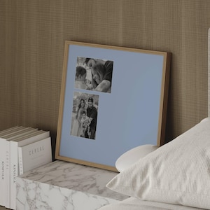 May include: A square wooden picture frame with a light blue mount featuring two black and white photographs. The top photo shows a person holding a child, and the bottom photo shows a group of three people standing together outdoors.