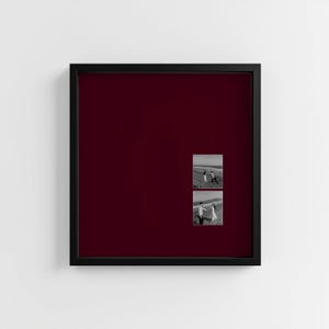 May include: A black framed photo collage with a deep burgundy background. Two small black and white photographs are displayed, showing people on a beach. The frame is square and mounted on a white wall.