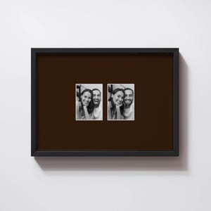 May include: A black rectangular picture frame with a dark brown matting. The frame holds two small black and white photographs of smiling people. The photographs are side by side, with a white border around each image.