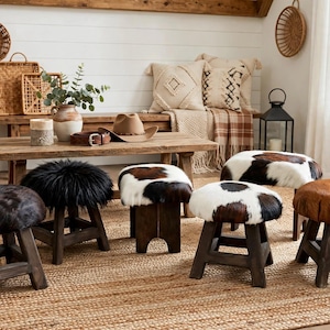 May include: A collection of six small wooden stools with round seats, featuring various upholstery styles including black faux fur, brown and white cowhide, and solid brown leather, all supported by dark stained wooden legs.