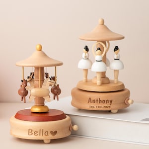 Puede incluir: Dos cajas de música de madera con diseños de carrusel. Una presenta caballos, la otra bailarinas. Las cajas de música son de color marrón claro con una base marrón oscuro. Una está grabada con "Bella" y la otra con "Anthony Sep. 12th, 2025".