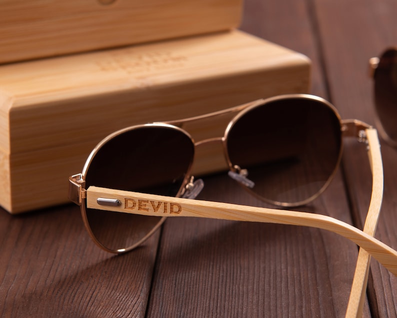 Puede incluir: Gafas de sol aviador marrones con montura dorada y patillas de bamb&uacute;. Las gafas tienen lentes de degradado marr&oacute;n y las palabras "DEVID" est&aacute;n grabadas en la patilla derecha.