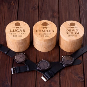 Pu&ograve; includere: Tre scatole di legno con testo inciso e un piccolo disegno di cappello. Le scatole sono etichettate "Lucas - Best Man Est 2022", "Charles - Groomsmen Est 2022" e "Devid - Groom Est 2022".
