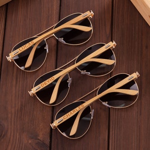Puede incluir: Tres pares de gafas de sol aviador marrones con monturas de madera. Cada montura est&aacute; grabada con un nombre diferente: Lucas, Devid y Charles.