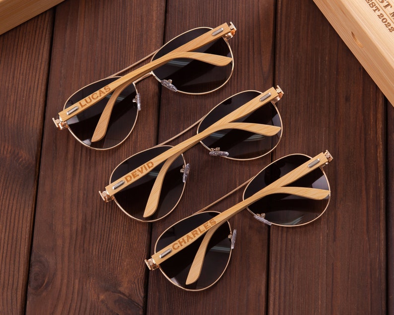 Puede incluir: Tres pares de gafas de sol aviador marrones con monturas de madera. Cada montura est&aacute; grabada con un nombre diferente: Lucas, Devid y Charles.