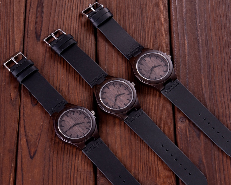 Pu&ograve; includere: Tre orologi da polso in legno con cinturini in pelle nera. Gli orologi hanno quadranti in legno marrone con lancette e indici neri.