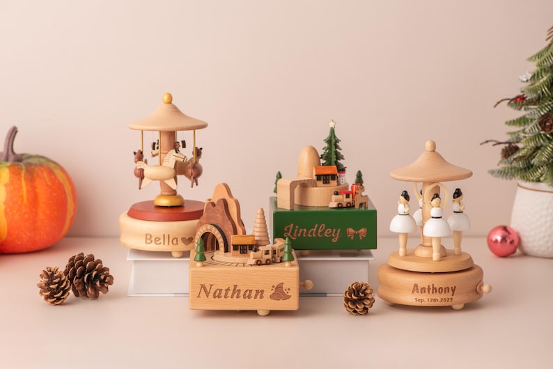 K&ouml;nnte beinhalten: Eine Sammlung von Holzspieluhren mit Karussell-, Zug- und Ballerina-Motiven. Die Spieluhren haben verschiedene Formen und Gr&ouml;&szlig;en und sind mit Namen graviert. Ein K&uuml;rbis, Tannenzapfen und ein kleiner Weihnachtsbaum sind ebenfalls im Bild.