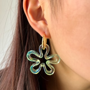 Puede incluir: Un par de pendientes de color verde iridiscente en forma de flor con un aro dorado.