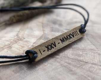 May include: A black cord bracelet with a wooden tag that says "I-XXV-MMXVIII".