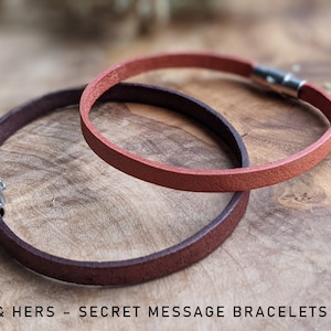 May include: Two leather bracelets with silver clasps. The bracelets are brown and orange.  "His & Hers - Secret Message Bracelets" is written below the bracelets.