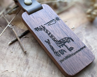 May include: A wooden keychain with a dark brown leather strap. The keychain features a laser-engraved design of two giraffes with a sun and clouds in the background.