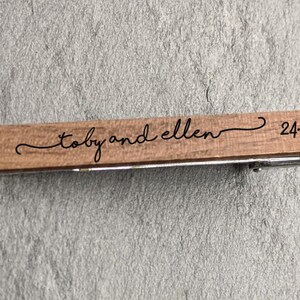 May include: A wooden tie clip with the text "Toby and Ellen" and the date "24.07.21" engraved on it.