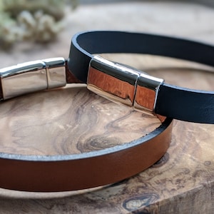May include: Two leather bracelets with silver magnetic clasps. One bracelet is brown leather and the other is black leather.