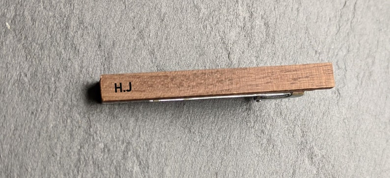 May include: A wooden tie bar with the initials "H.J." engraved on it.