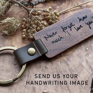 Könnte beinhalten: Ein brauner Holzschlüsselanhänger mit einem Lederband und einem Messing-Schlüsselring. Das Holz ist mit der handschriftlichen Nachricht "Never forget how much I love you!" graviert.