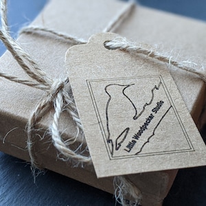 May include: A brown cardboard box with a brown paper tag tied with twine. The tag has a black and white illustration of a bird and the text "Little Woodpecker Studio".