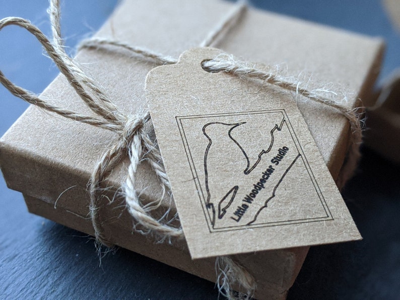May include: A brown cardboard box with a brown paper tag tied with twine. The tag has a black and white illustration of a bird and the text "Little Woodpecker Studio".