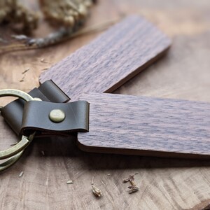 Puede incluir: Un llavero de madera con una correa de cuero marr&oacute;n y un anillo de llave de lat&oacute;n. La madera tiene un color marr&oacute;n oscuro con un patr&oacute;n de veta natural.