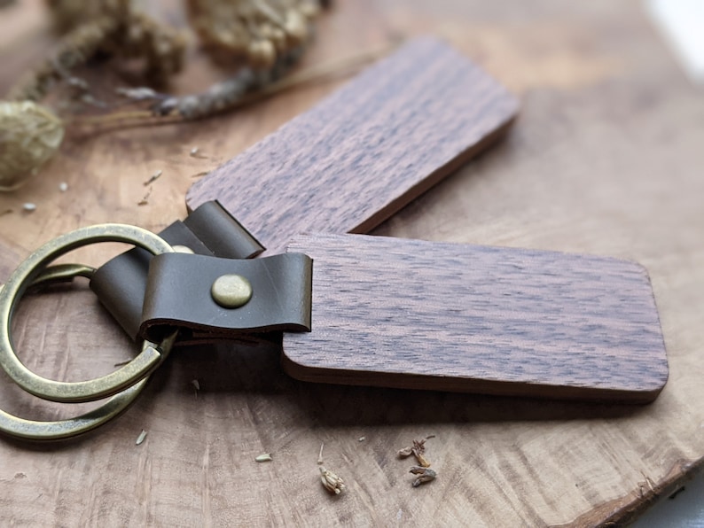 Puede incluir: Un llavero de madera con una correa de cuero marr&oacute;n y un anillo de llave de lat&oacute;n. La madera tiene un color marr&oacute;n oscuro con un patr&oacute;n de veta natural.