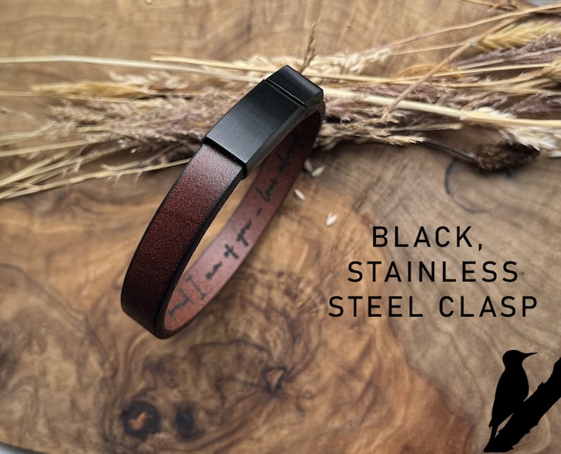 May include: A brown leather bracelet with a black stainless steel clasp. The bracelet has the text "I am free - Love is free" engraved on it.