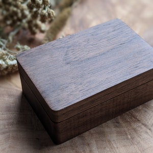 May include: A dark brown wooden box with a hinged lid. The box has a smooth, polished finish and is made of a high-quality wood.