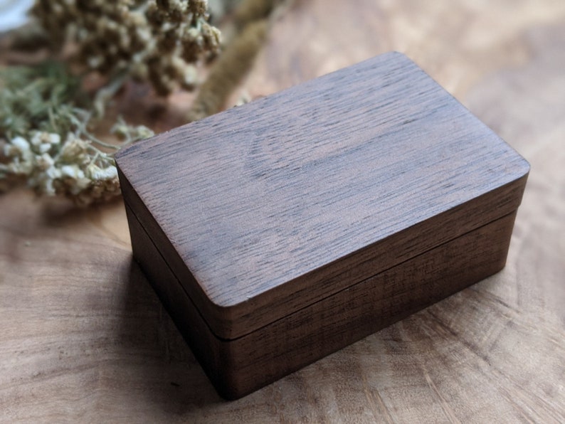May include: A dark brown wooden box with a hinged lid. The box has a smooth, polished finish and is made of a high-quality wood.