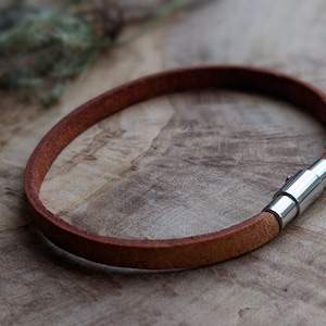May include: A brown leather bracelet with a silver metal clasp.