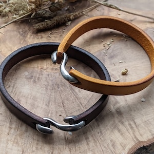 May include: Two leather bracelets with silver clasps. One bracelet is brown and the other is tan.