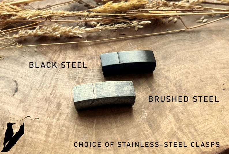 May include: Two stainless steel clasps, one black and one brushed steel, are displayed on a wooden surface. The text "BLACK STEEL" and "BRUSHED STEEL" are above each clasp. The text "CHOICE OF STAINLESS-STEEL CLASPS" is below.